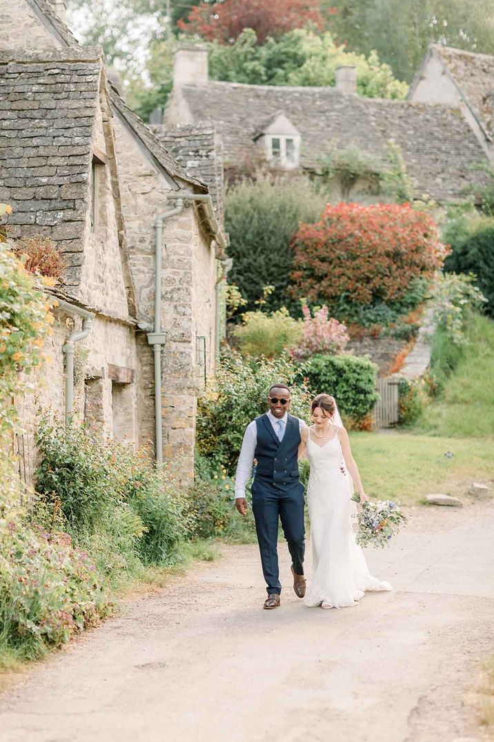 Bride and groom walk hand in hand through the Cotswolds at their traditional wedding