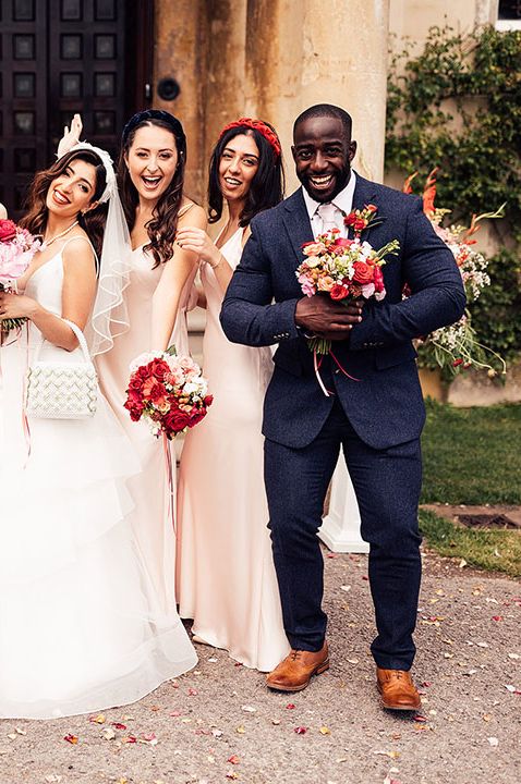 Bride in tulle skirt wedding dress with bouquet and bridesmaids in pink satin bridesmaid dresses, man in blue suit 