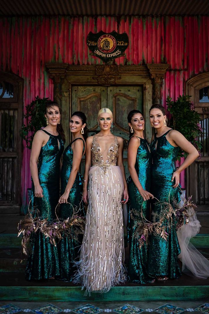 Bridesmaids in emerald green sequinned bridesmaid dresses with halter neck and cutout for festival wedding with bride in gold wedding dress