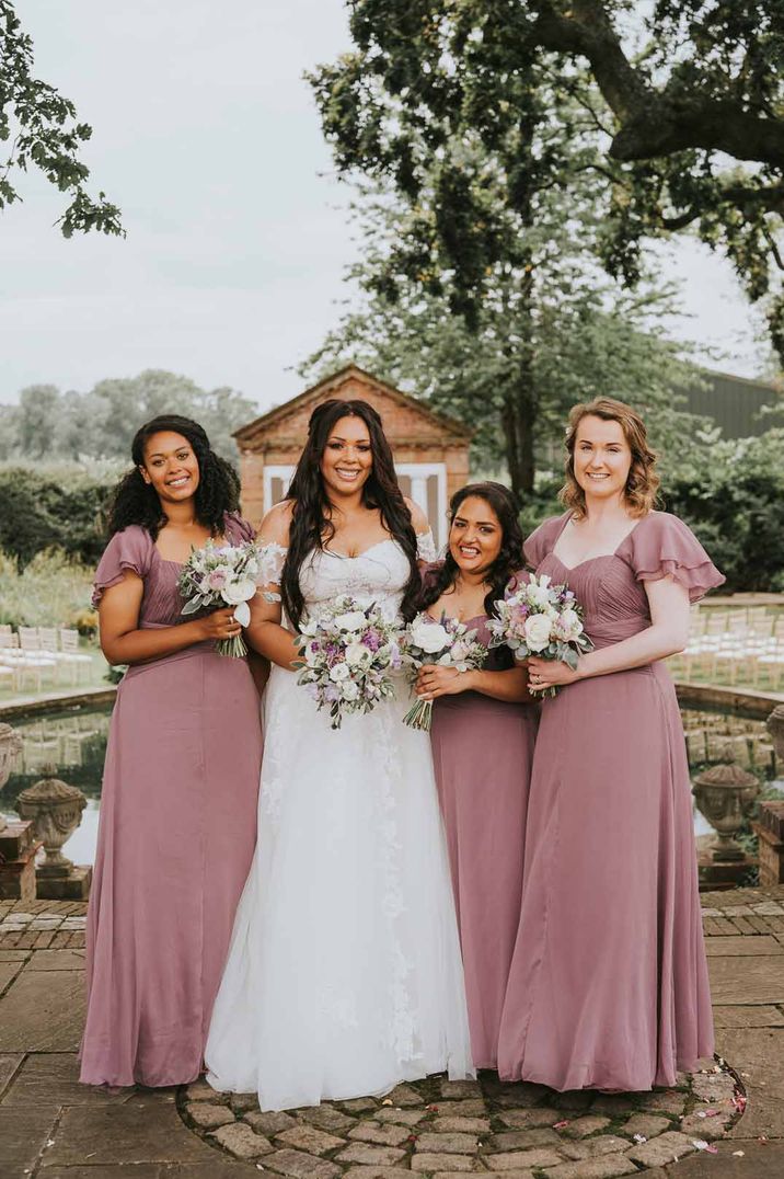 Bride in off the shoulder lace wedding dress standing with bridesmaids in square neck short sleeve dusky pink bridesmaid dresses 