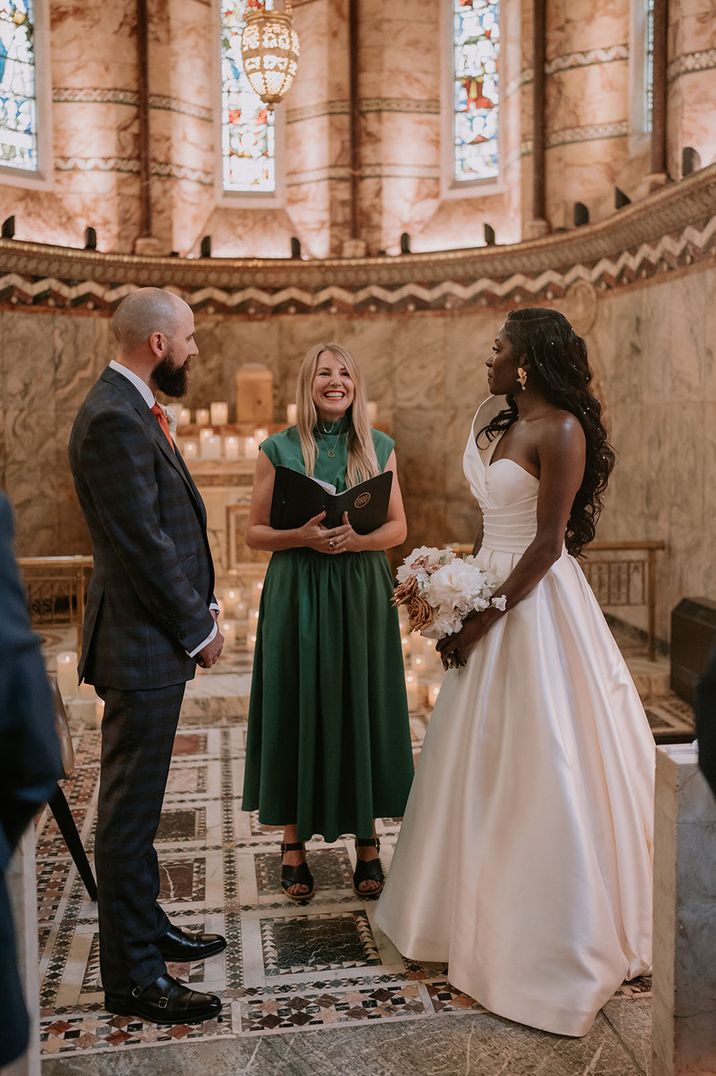 Roxy Celebrates Love performing as wedding celebrant for groom in grey checkered suit with an orange tie and Black bride in strapless gown