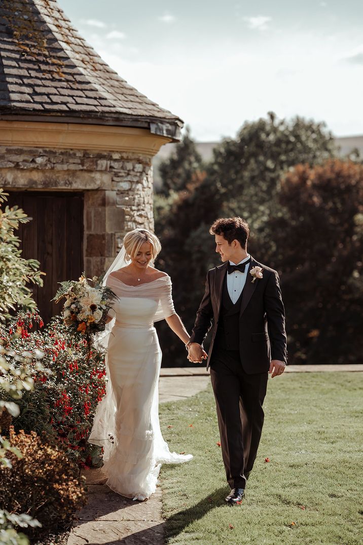 Bride in off the shoulder wedding dress walking with the groom around their Yorkshire wedding venue 