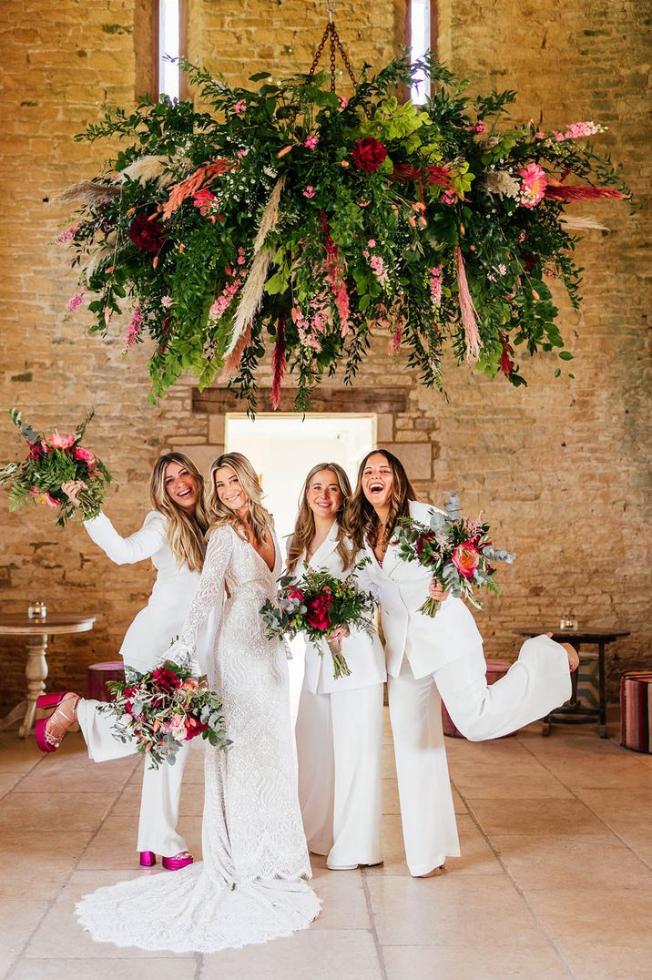 Bridal party in white jumpsuits with the bride under colourful pink flower hanging installation 