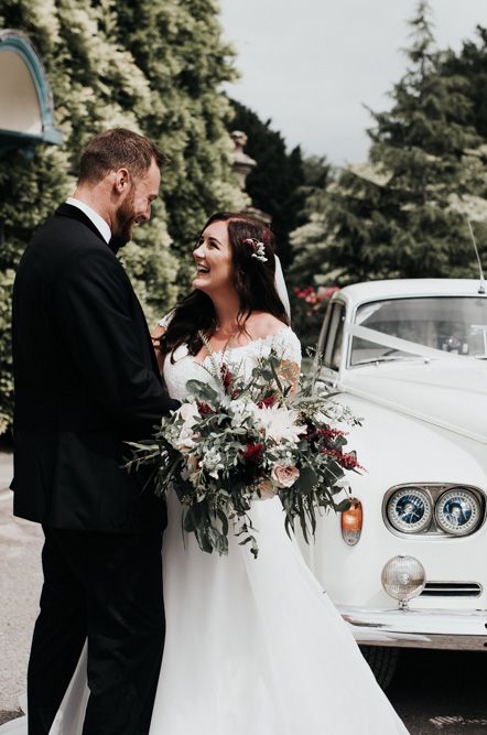 Bride in off the shoulder dress and groom standing by a white Rolls Royce wedding car