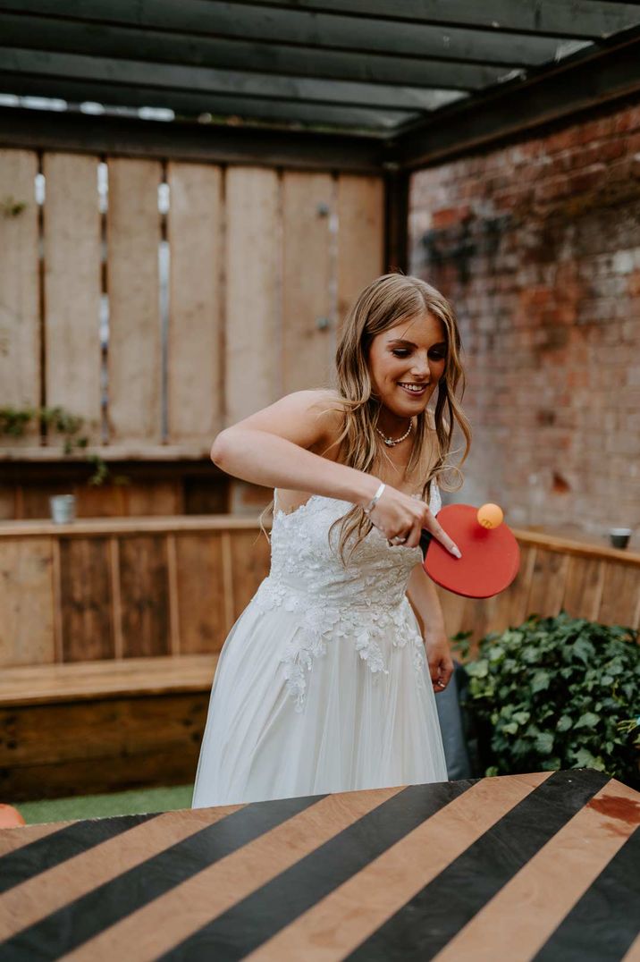 Bride in embellished top strapless wedding dress playing ping pong at The Shack Revolution