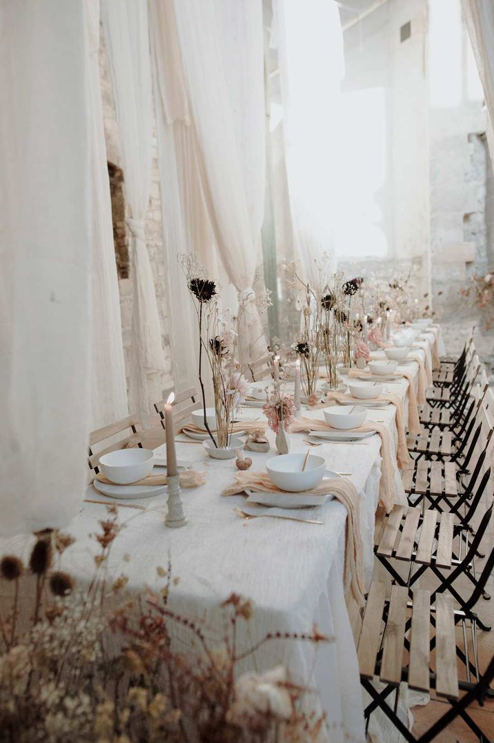 Neutral white minimal wedding tablescape with white table cloth, pink tulle napkins, black stems in vases and neutral tapered candles 