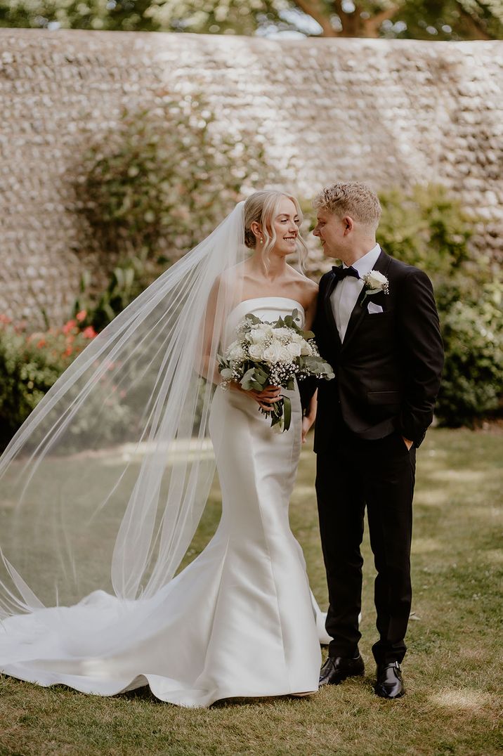 Bride in strapless wedding dress and veil with groom in black tuxedo for classic wedding 