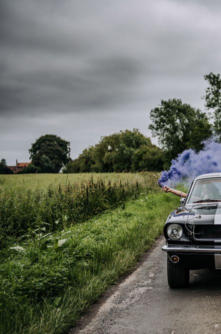 Smoke bomb portrait with the bride and groom holding blue grenades out the windows of their Ford Mustang wedding car 