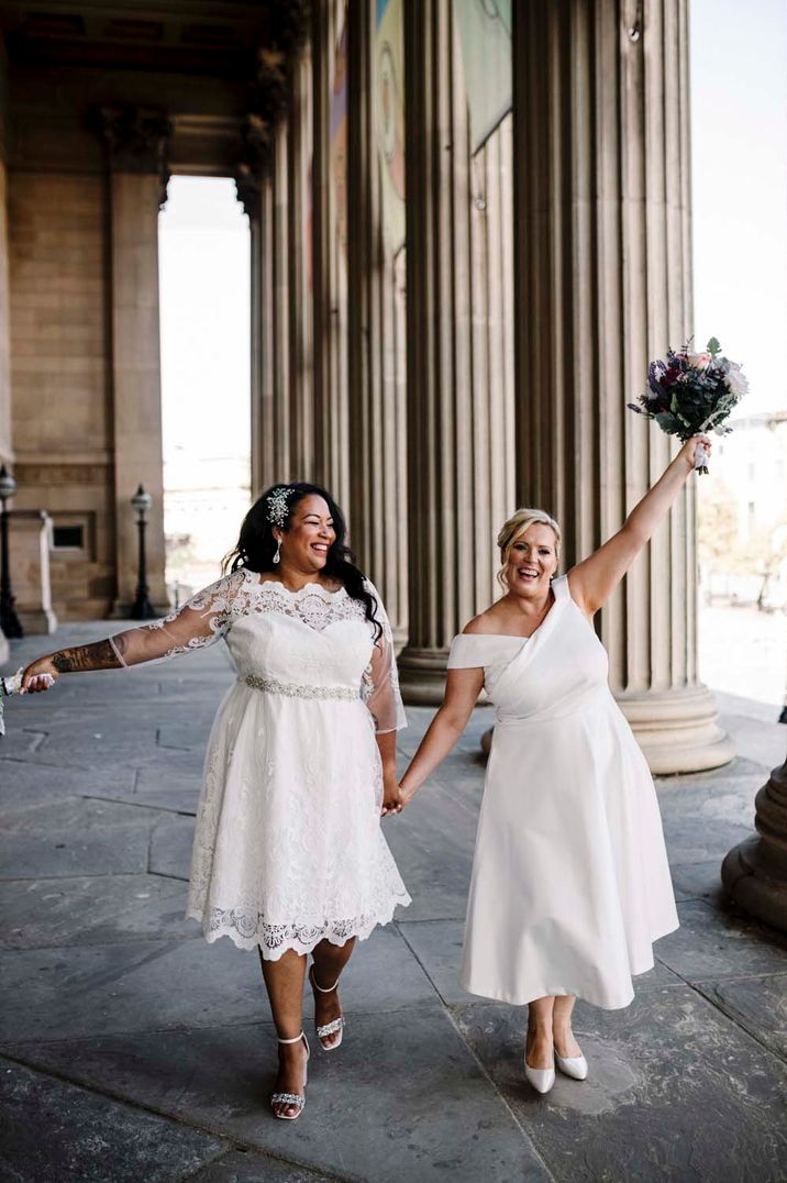 St George's Hall Liverpool wedding with two brides in tea length wedding dresses holding their bouquets in the air 