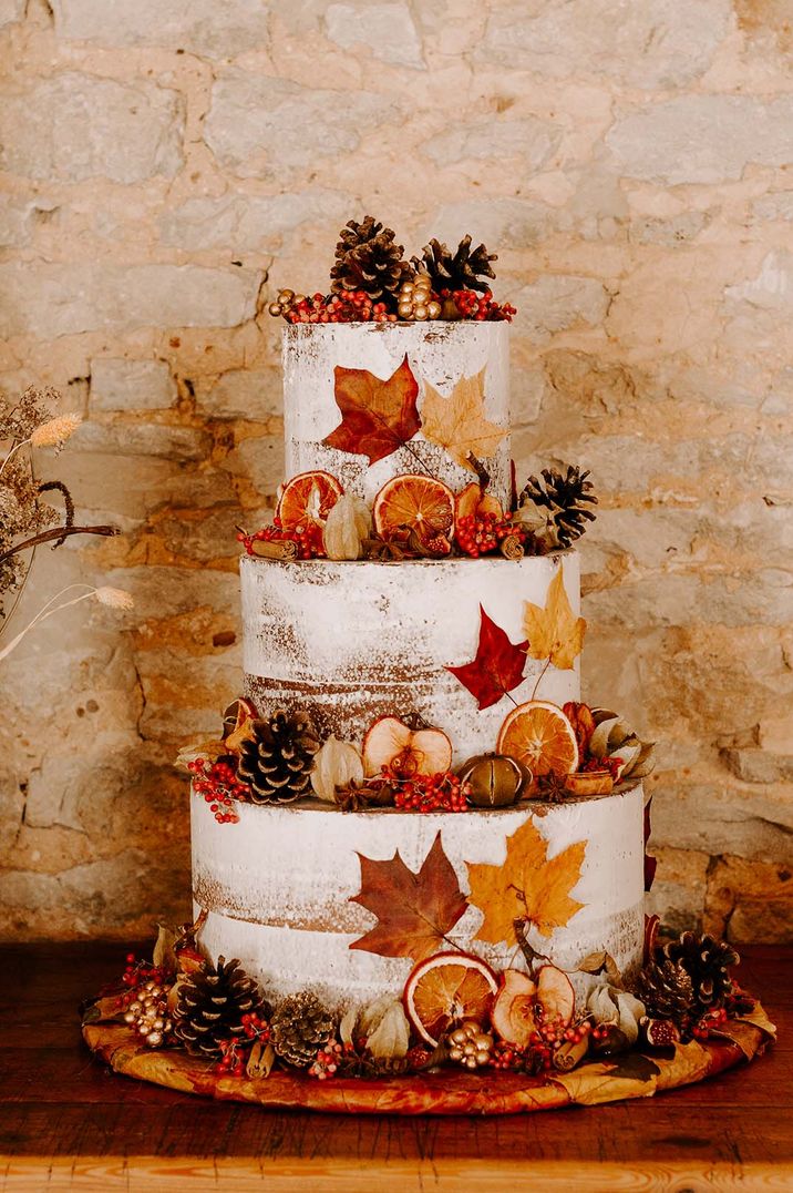 Three tier wedding cake with white frosting and autumnal leaf decorations