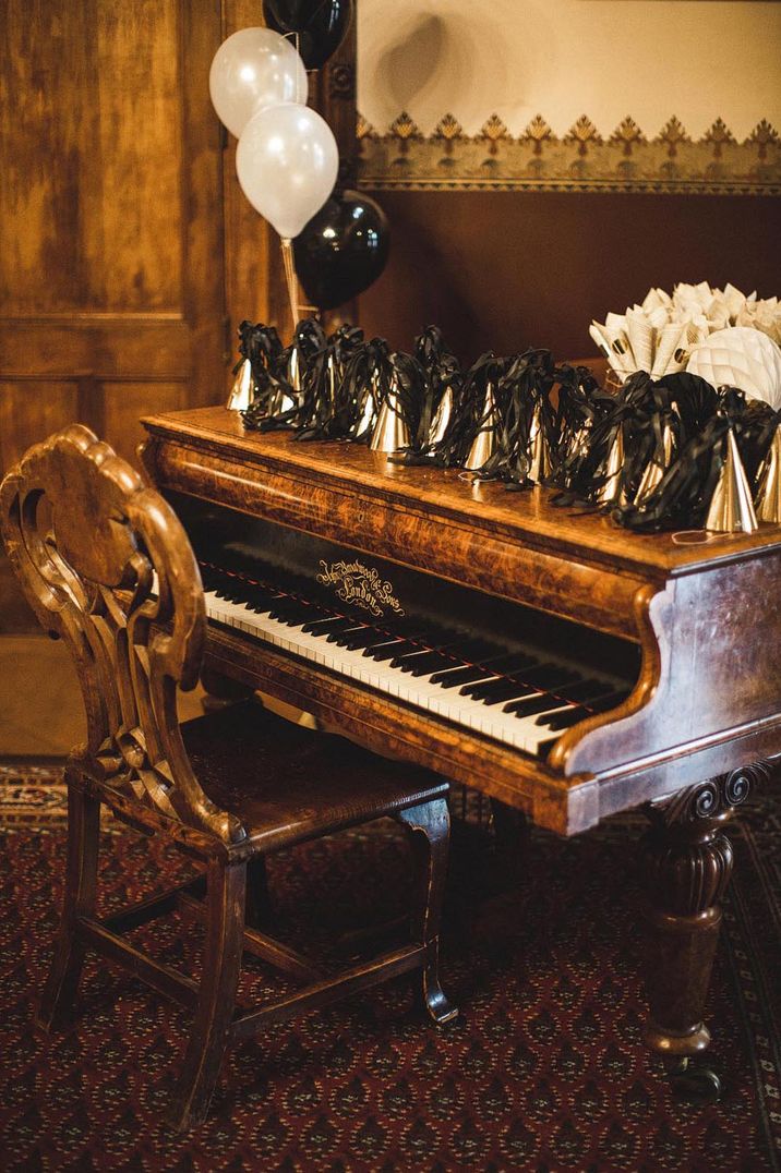 Piano decorated with black and gold wedding party hats, confetti and balloons