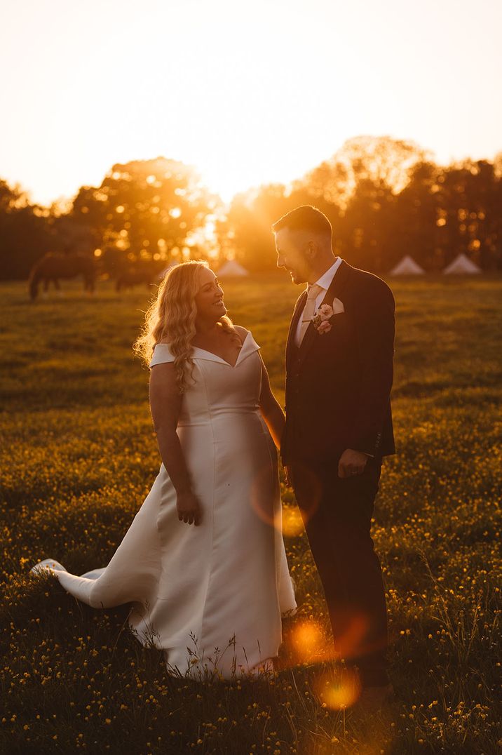 Bride and groom posing together at sunset filled with air golden lighting 