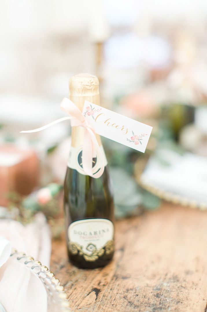 Mini bottle of champagne with pale pink flowers on the favour tag saying 'cheers' 