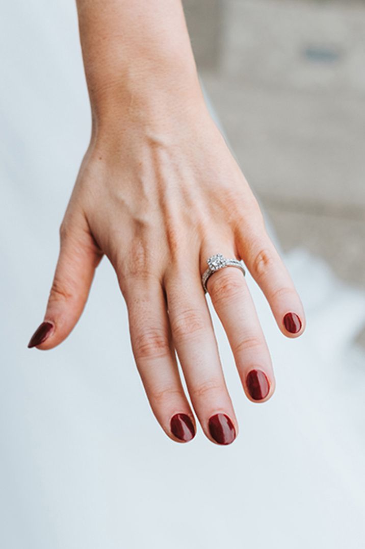 Rounded burgundy nails with round halo silver engagement ring 