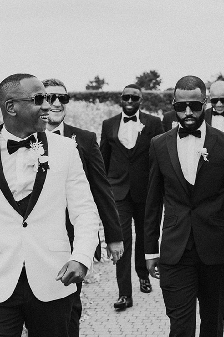 Groom in white tuxedo walking with groomsmen in tuxedos and black sunglasses 