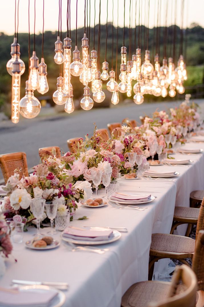 Pastel pink wedding theme with decorative Edison bulbs above the outdoor tablescape in Italy 