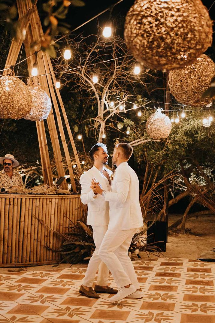 Two grooms in white suits at destination wedding dancing together on the dance floor 