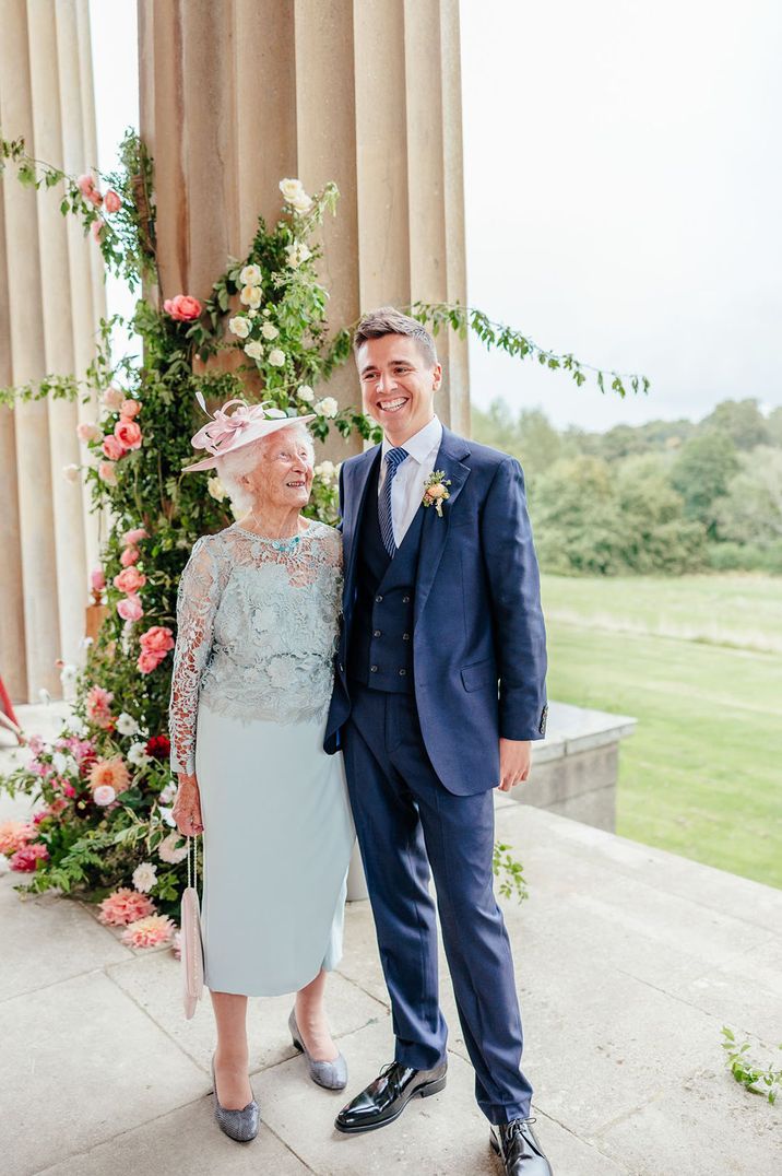 Groom posing with elderly wedding guest or grandparent wearing a pink wedding fascinator 