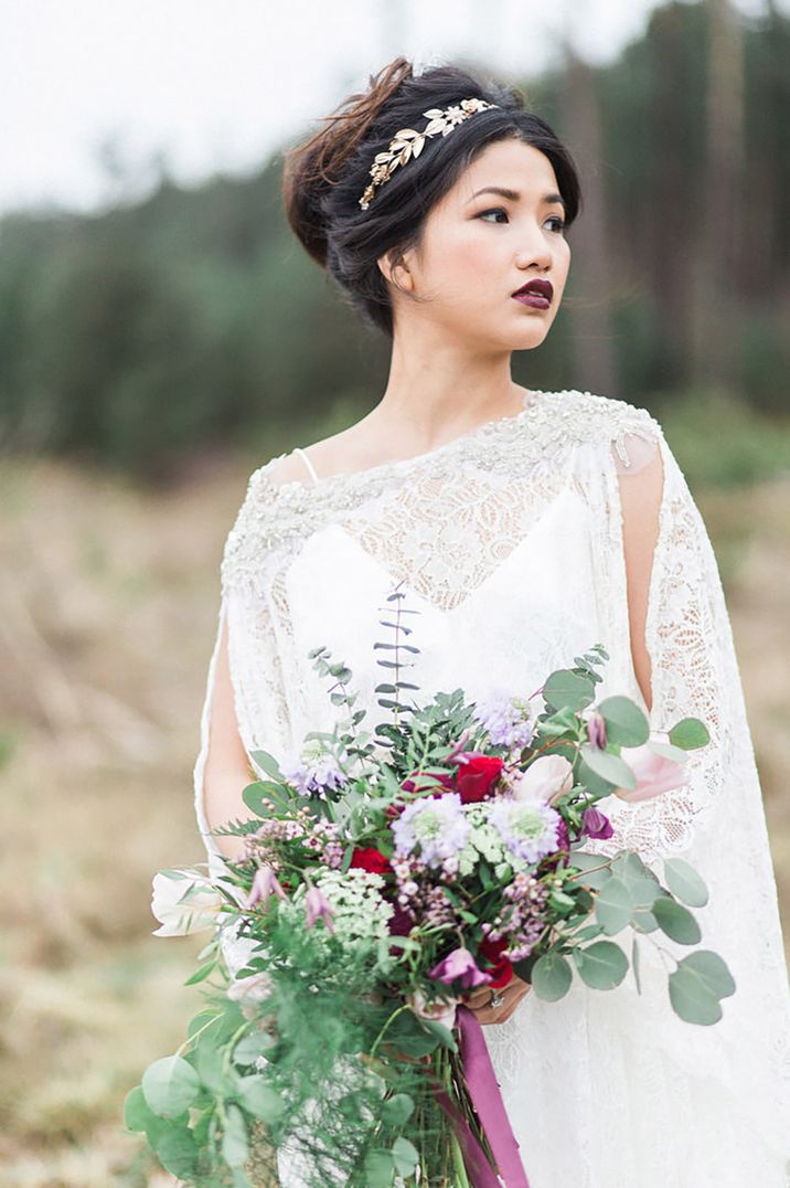 Bride with gold leaf crown accessory and dark lipstick wearing a lace cape 