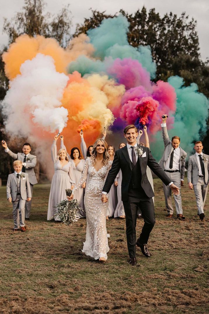 Colourful smoke bomb with bride in a fitted lace wedding dress and groom a navy suit