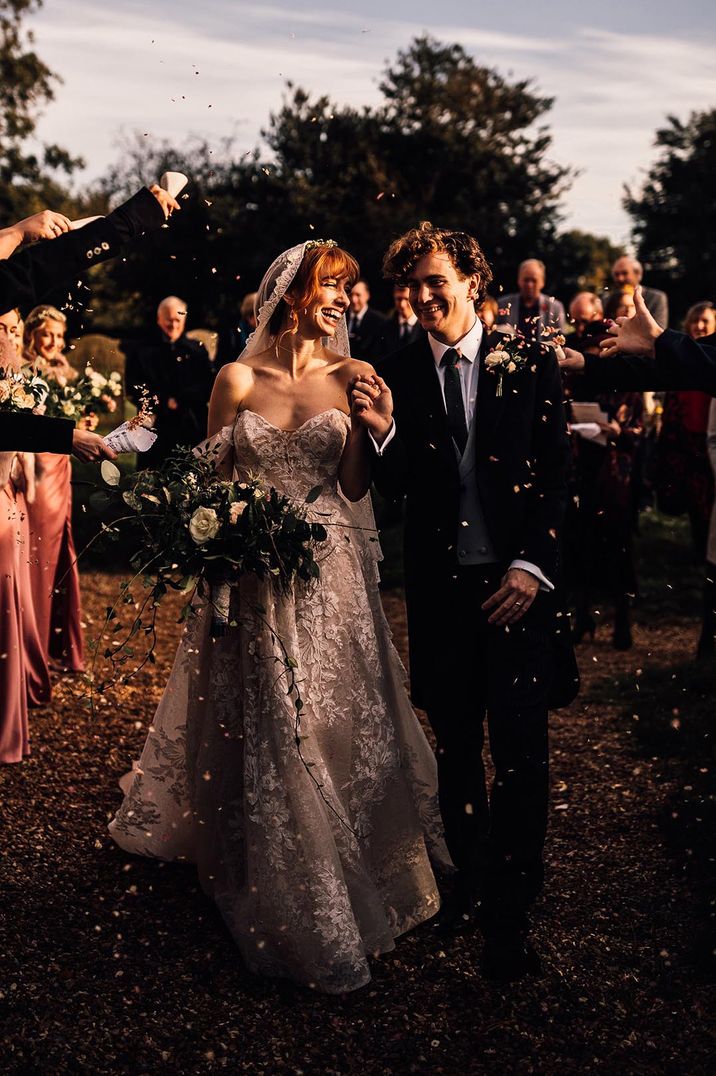 Bride in a strapless lace gown with an embroidered edge veil having a confetti moment with the groom 