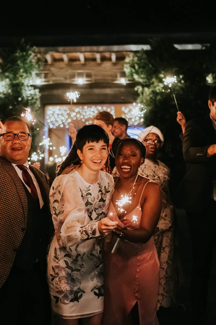 Two brides in their wedding reception dresses participate in their sparkler send off 