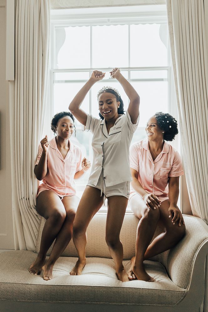 Bride in white getting ready pyjamas and bridesmaids in pink getting ready pyjamas dancing before wedding