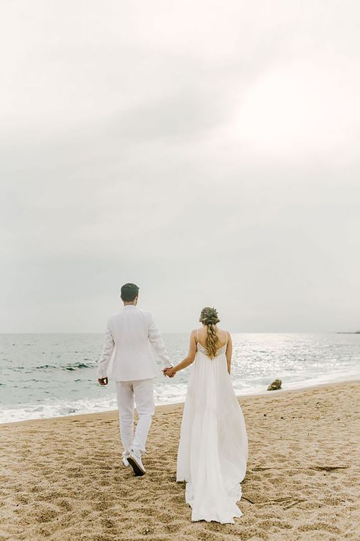 Bride and groom walking hand in hand on a beach for beach wedding ceremony with bride wearing a flowy beach wedding dress