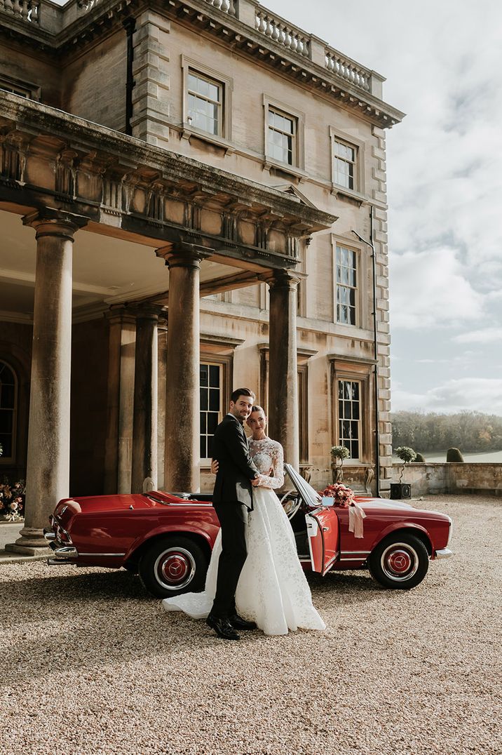 Red vintage wedding car outside of Prestwold Hall classic wedding venue with bride and groom in black tie attire 