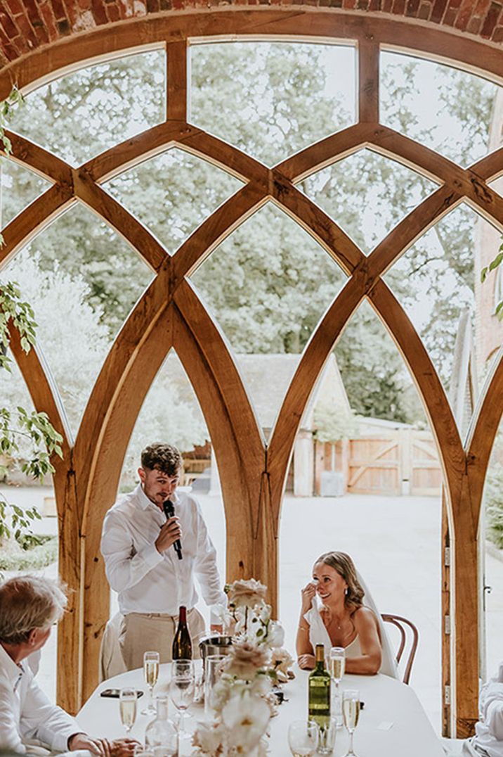 Stunning windows at Shustoke Farm Barns with the groom standing to read out his wedding speech 