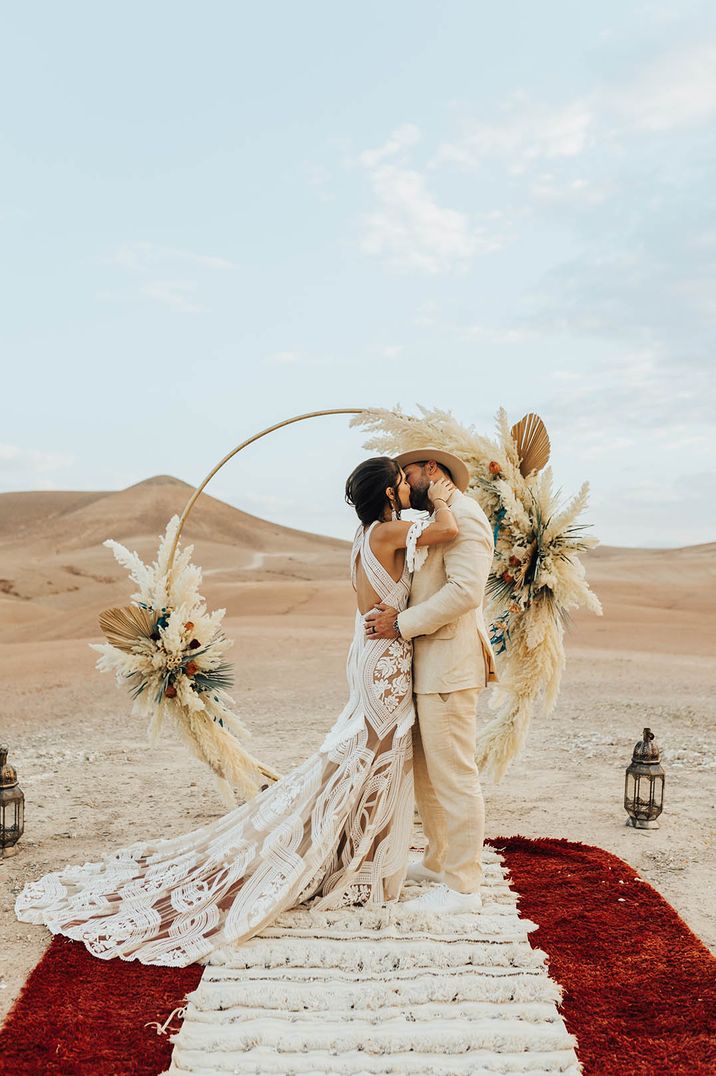 bride-in-boho-lace-wedding-dress-with-groom-in-beige-suit-sharing-first-kiss-as-married-couple