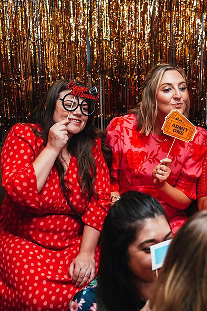 wedding guests in photo booth with props wearing red long sleeve wedding guest dresses