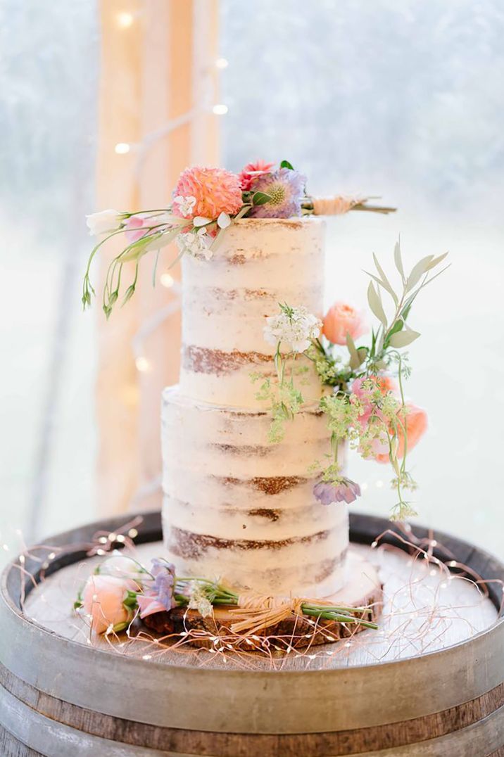 Tall tiered semi-naked rustic wedding cake decorated with pink and purple wedding cake decorations