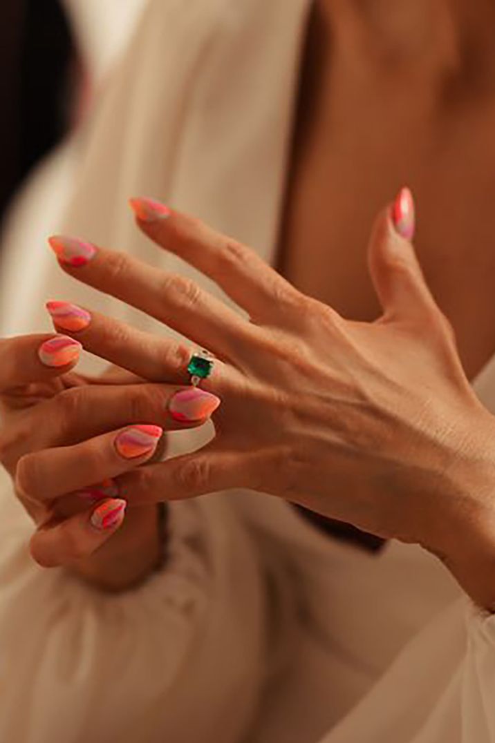 Bride wears almond shaped wedding nails with pink abstract wavy lines nail art with emerald engagement ring