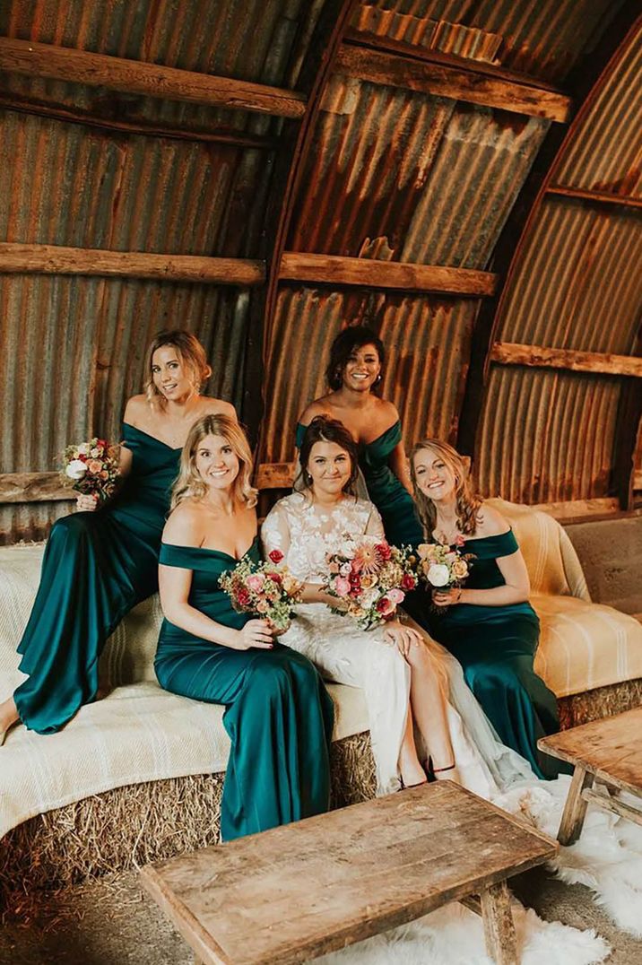 bride with bridesmaids wearing emerald green gemstone dresses in barn