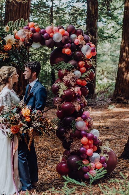 Bride and Groom Standing in Front of an Autumnal Flower and Balloon Arch