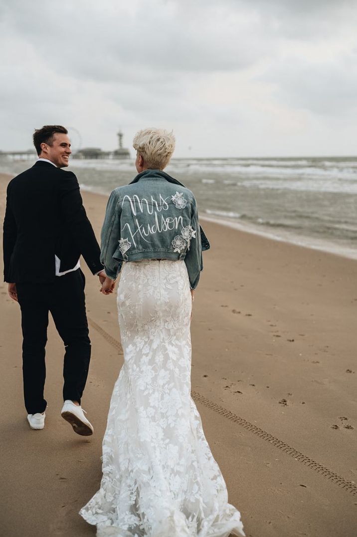 Bride and groom walking along their beach weddings with denim jacket