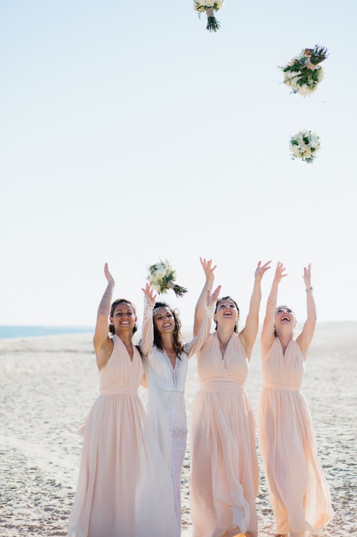 Bridesmaid throwing their bouquets in the air at beach wedding