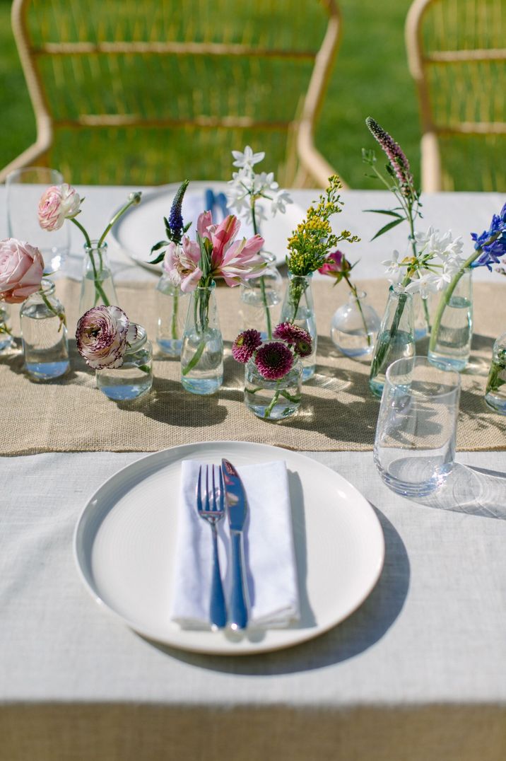 Wedding table place setting using single stems of vibrant spring flowers, oatmeal linen tablecloth and jute table runner