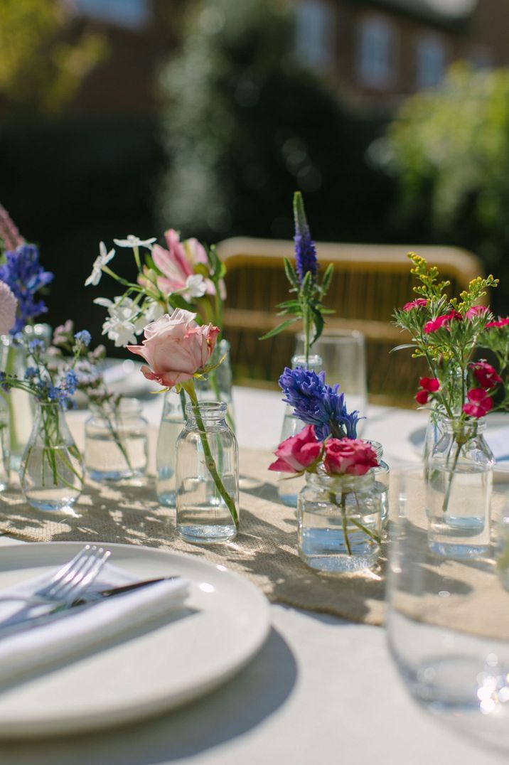 Floral wedding centrepiece for an outdoor garden wedding created using roses, mini chrysanthemums, wax flowers and ranunculus in mini glass vases