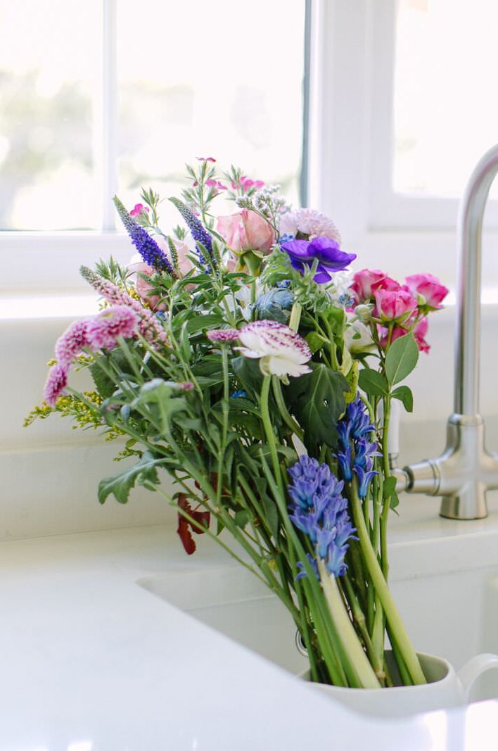 Bouquet of fresh spring flowers in vibrant shades of pinks, blues and purples, standing in an undermount ceramic sink