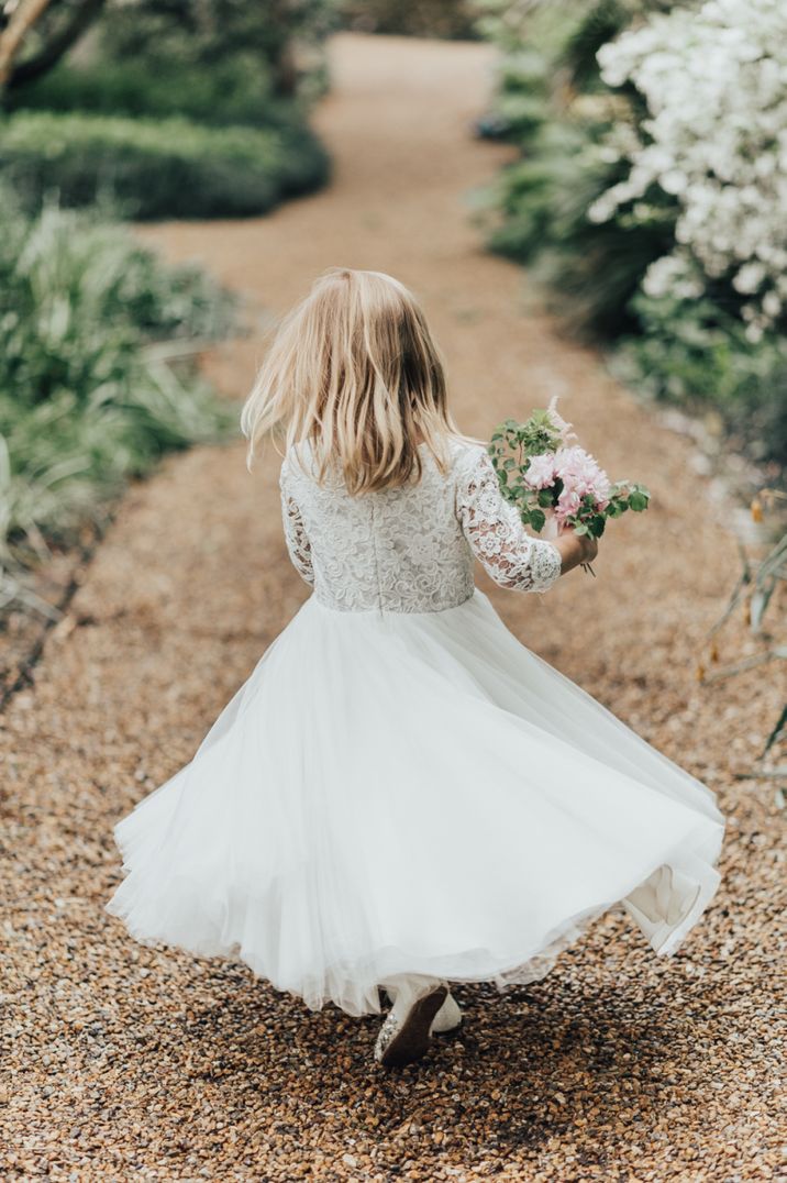 Flower girl in white dress twirling with flowers