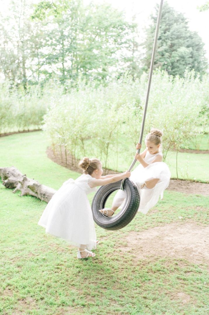 Flower girls in white dresses playing on a tyre swing