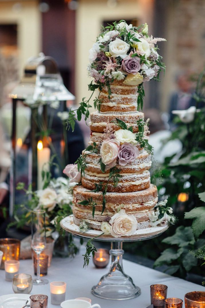 Four tiered naked wedding cake with no icing and lots of roses for decoration