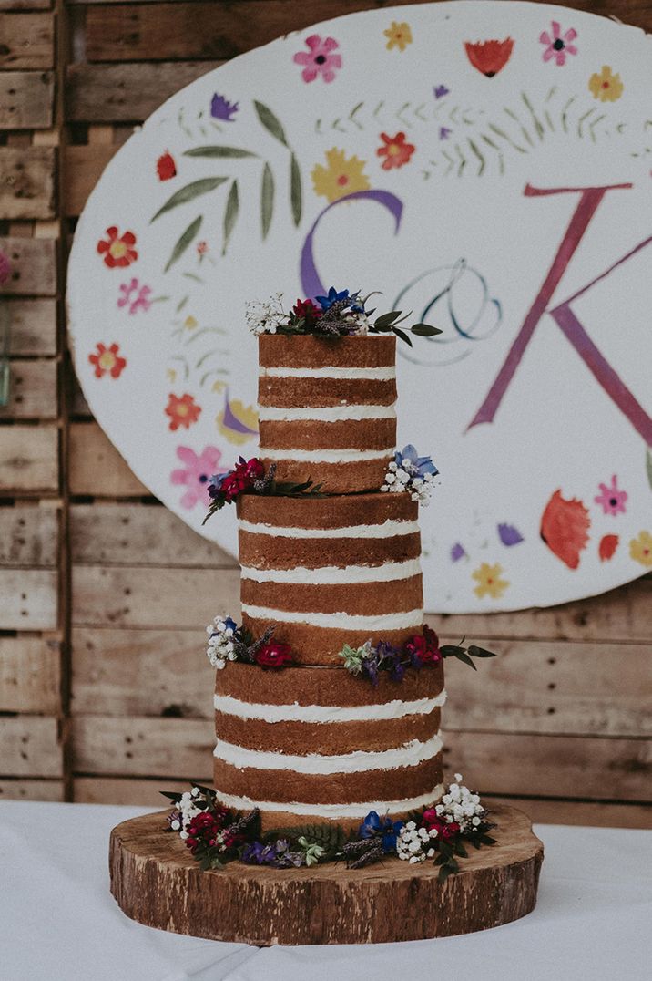 Three tall tier naked wedding cake with no icing decorated with wedding flowers