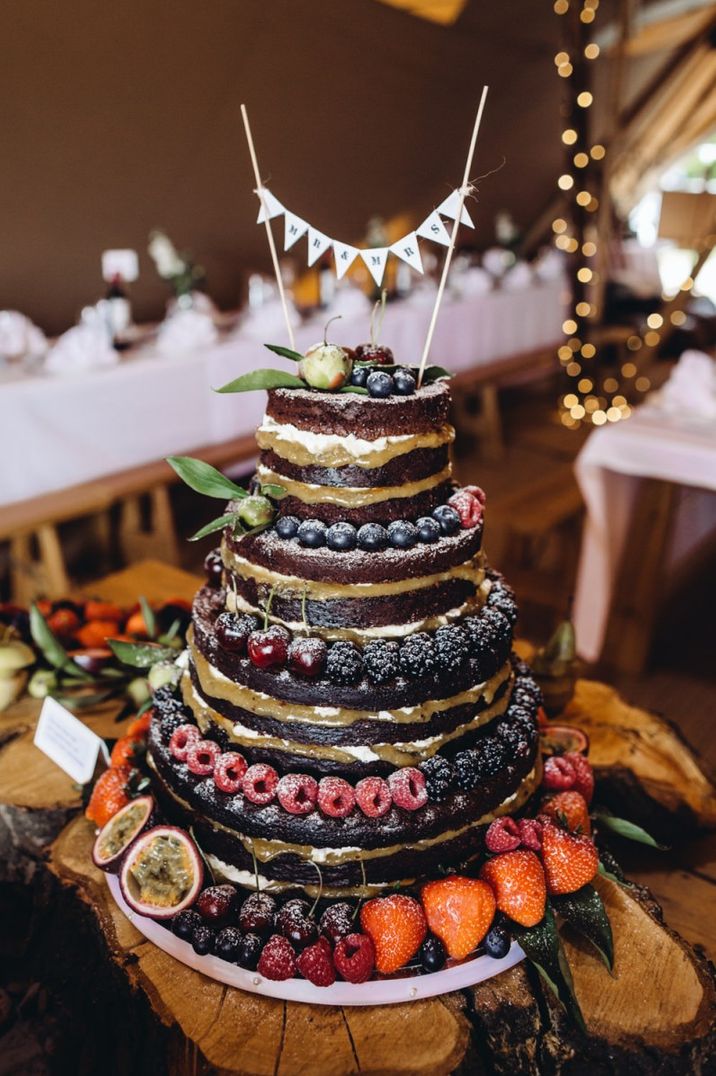 Five tier naked wedding cake decorated with berries between each tier and a bunting cake topper