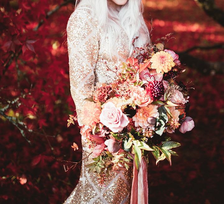 Bride with oversized bouquet stood in front on red trees. Photography by Maryanne Weddings.