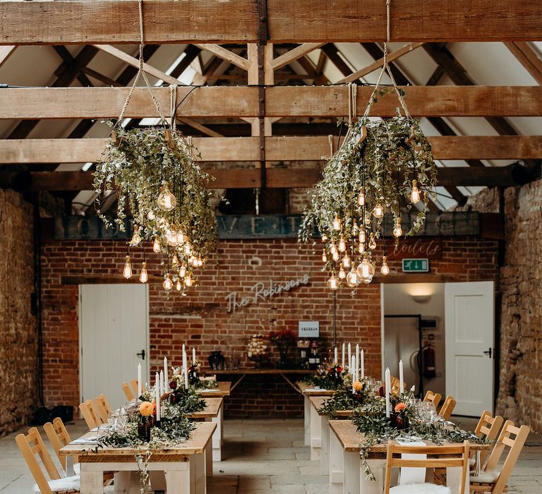 Barn reception venue with wooden tables, hanging ivy and lights