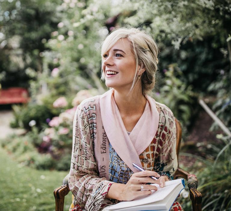 Bride on her wedding morning sitting in the garden writing a note in a getting ready robe 