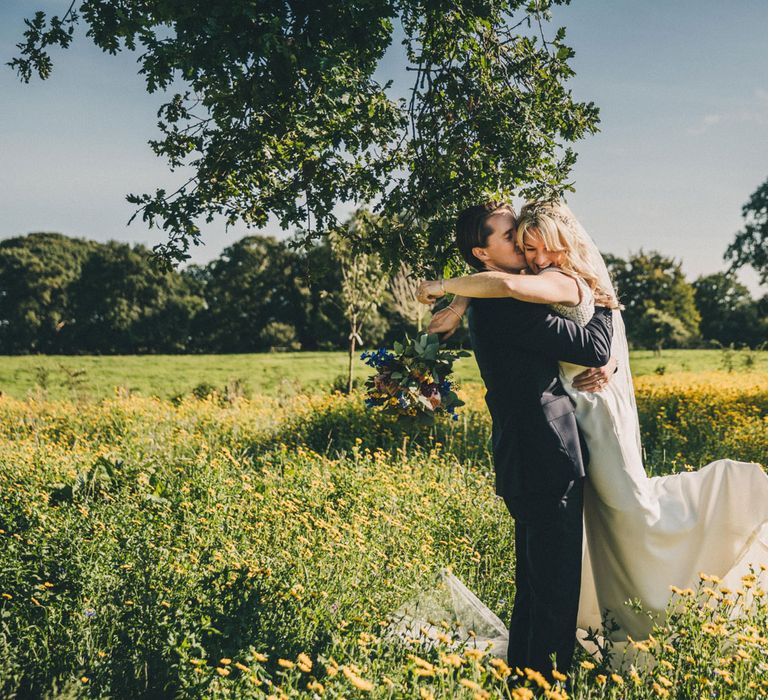 Smiling bride in Justin Alexander wedding dress hugs groom in meadow at Iscoyd Park wedding reception